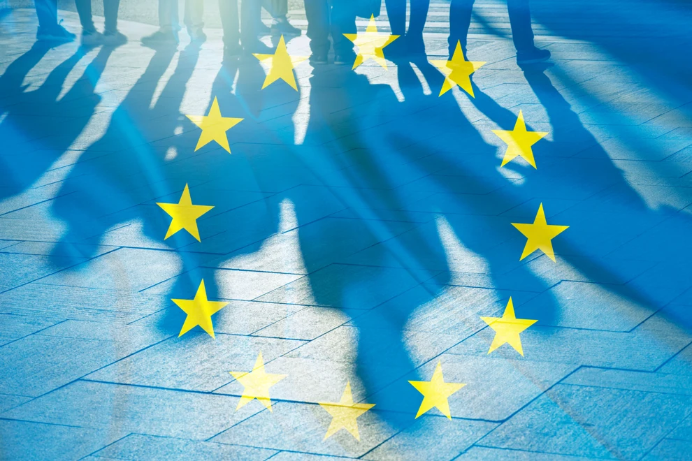 Skuggor av personer mot en EU-flagga.