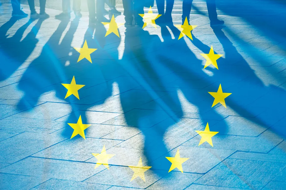Skuggor av personer mot en EU-flagga.